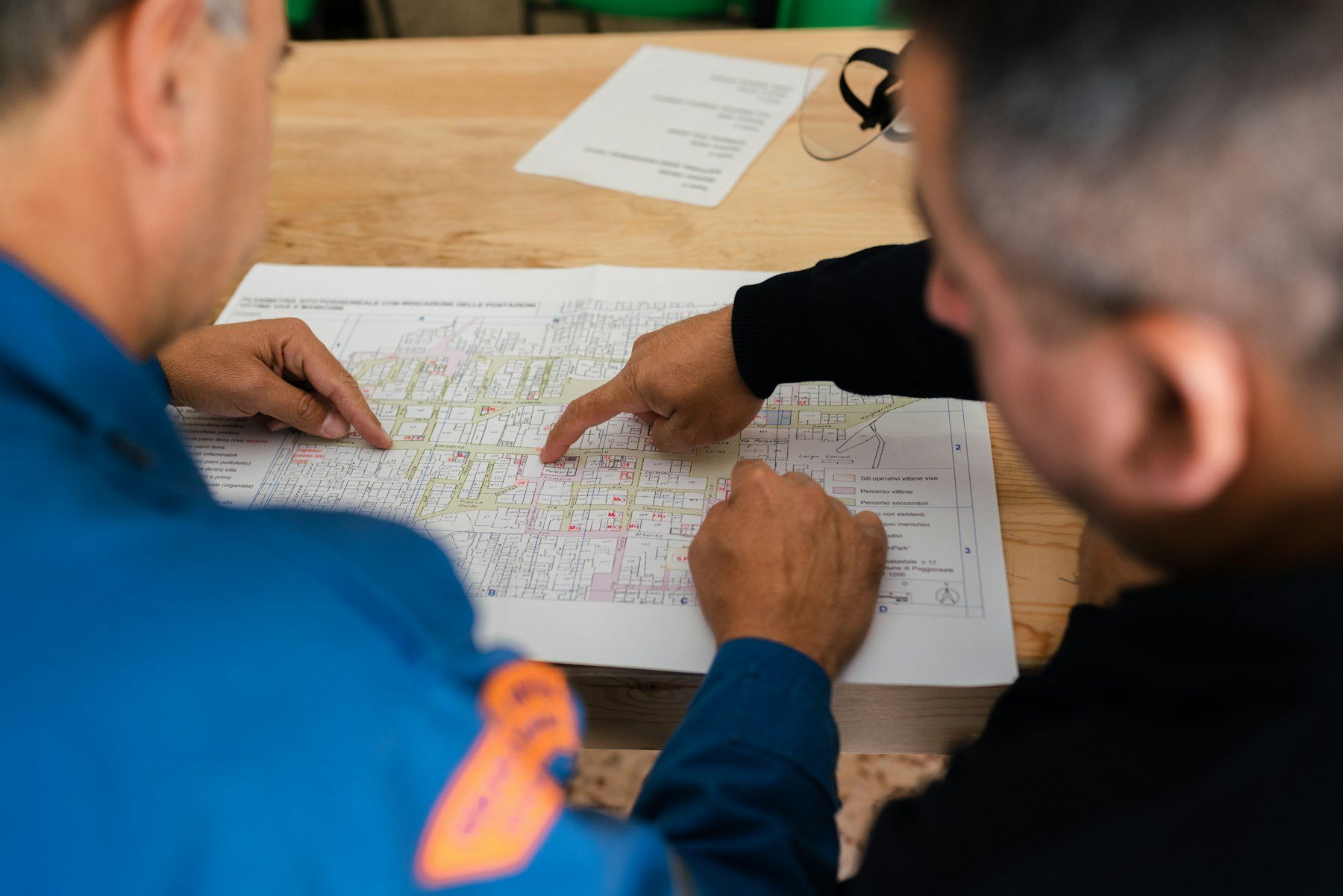 Two people in work uniforms going through technical documents together at a table.